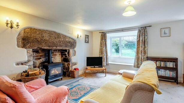 A cozy living room with a stone fireplace, a television, a bookshelf, and a large window. - 2 bedroom accommodation in Harford, Dartmoor National Park (Harford, Dartmoor National Park)