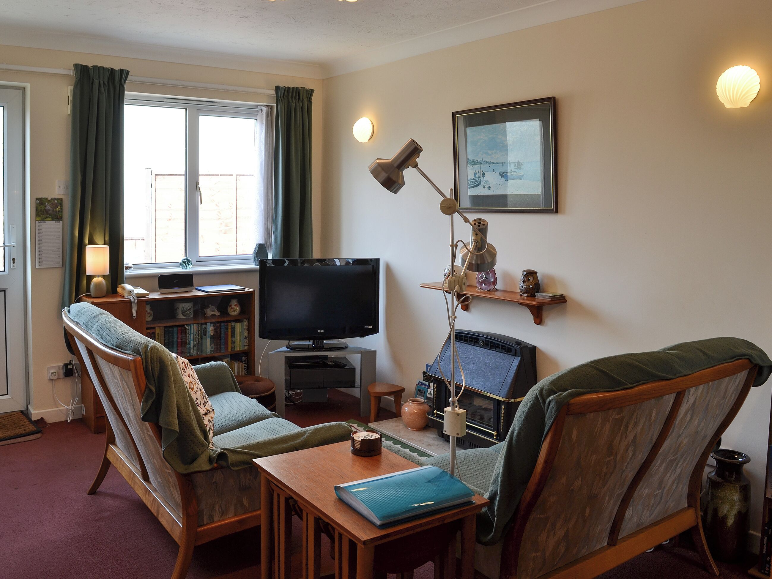 Een woonkamer met een televisie, twee fauteuils, een houten salontafel, een boekenkast en een raam met gordijnen.