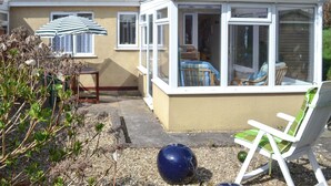 A conservatory with a glass roof, a chair, and a table outside a house. - 2 bedroom accommodation in Chivenor Cross, near Barnstaple (Chivenor Cross, near Barnstaple)