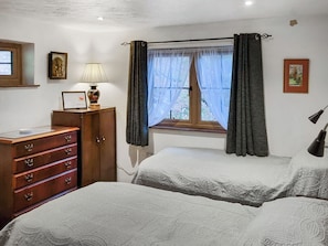 A bedroom with two beds, a wooden dresser, a window with curtains, and a lamp.