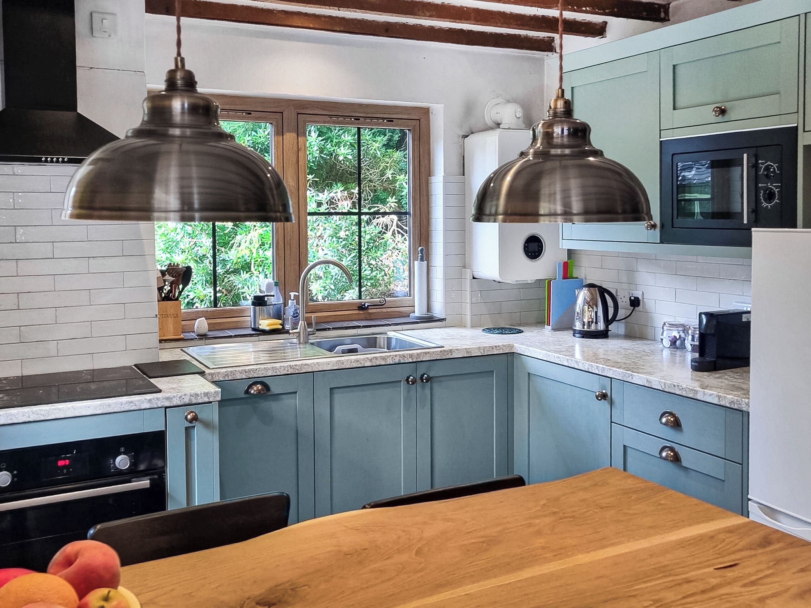A kitchen with blue cabinets, a wooden table, and a window with greenery outside.