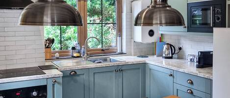 A kitchen with blue cabinets, a wooden table, and a window with greenery outside.
