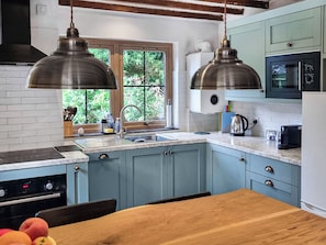 Une cuisine avec des meubles de couleur bleue, une table en bois et une fenêtre donnant sur un espace verdoyant.