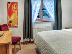 Une chambre à coucher avec un lit, un bureau, une chaise, un radiateur et une fenêtre avec des rideaux.