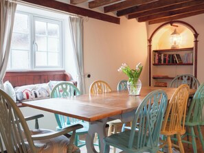 A dining area with a wooden table, teal chairs, a vase with flowers, a bookshelf, and a window with curtains. - 4 bedroom accommodation in Docking, near Hunstanton (Docking, near Hunstanton)