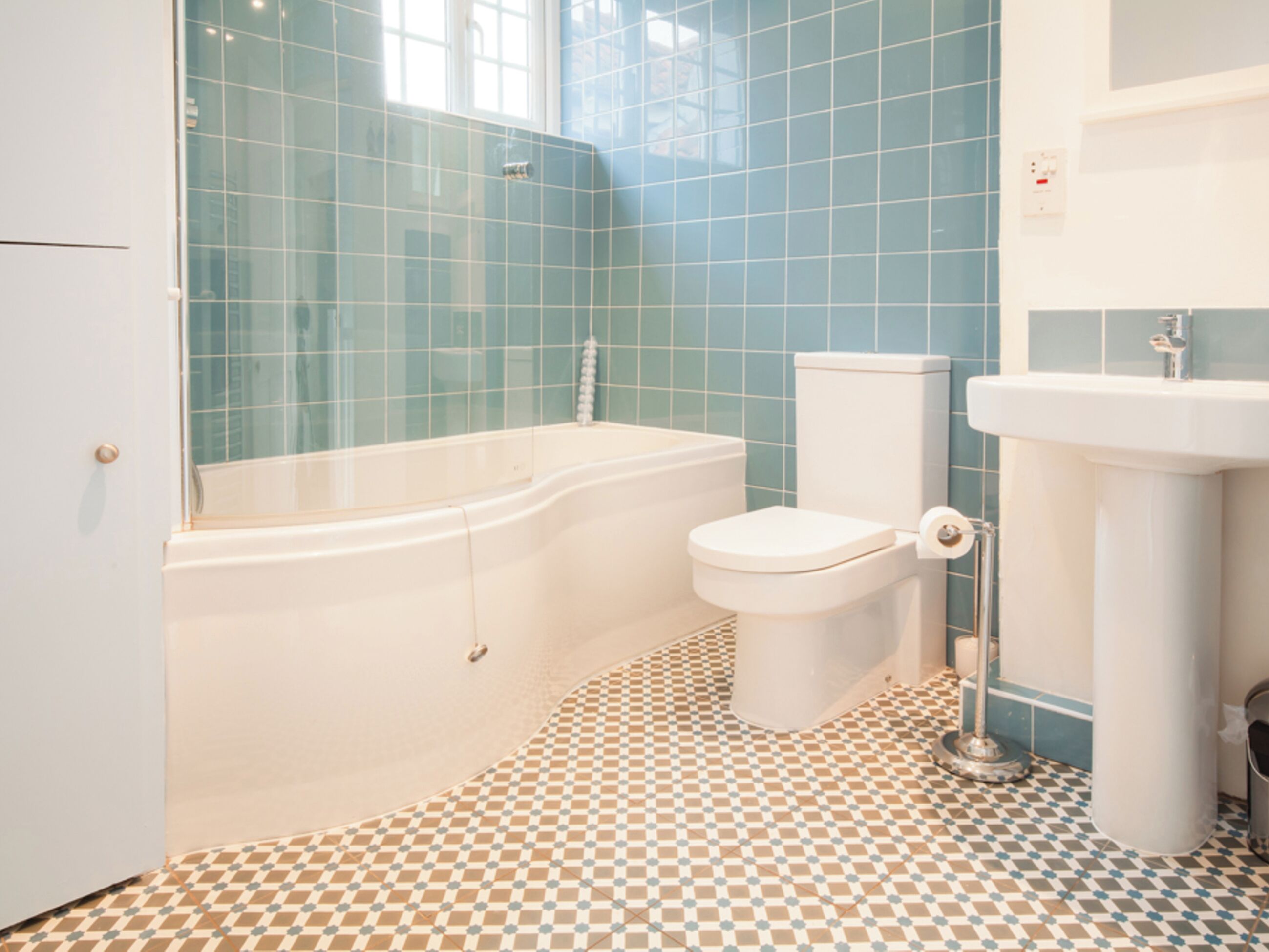 A bathroom with a bathtub, toilet, and sink, featuring blue tiles and a checkered floor pattern.
