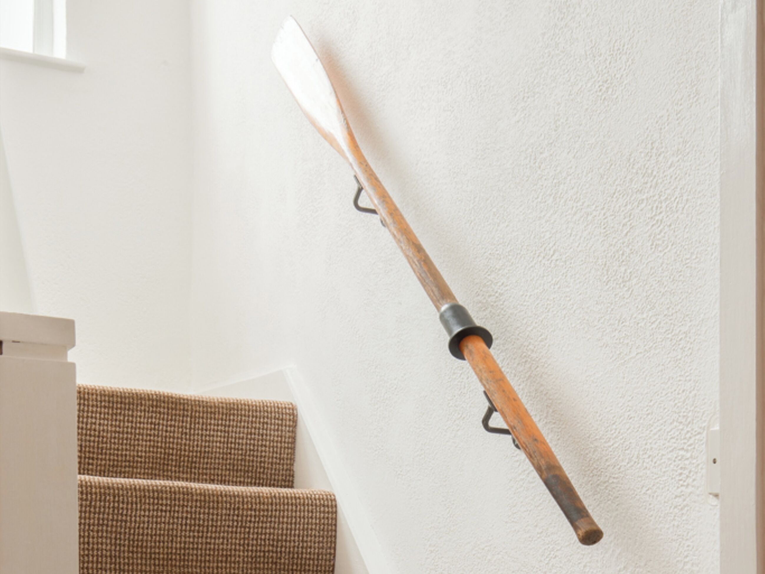 A wooden paddle leaning against a white wall, a staircase with brown steps, and a white door frame.