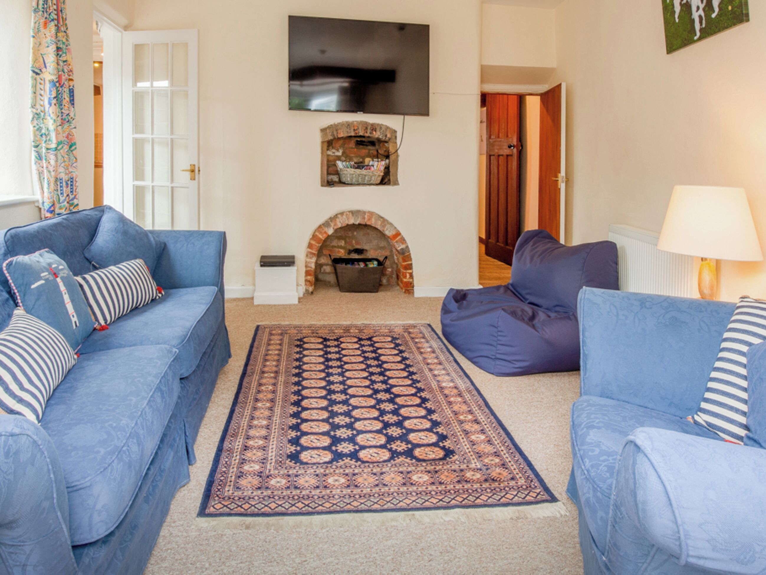 A living room with two blue sofas, a patterned rug, a fireplace, and a television on the wall.