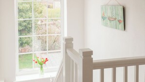 Quarto com corrimão branco, janela com vista para o verde e um adorno pendurado na parede.