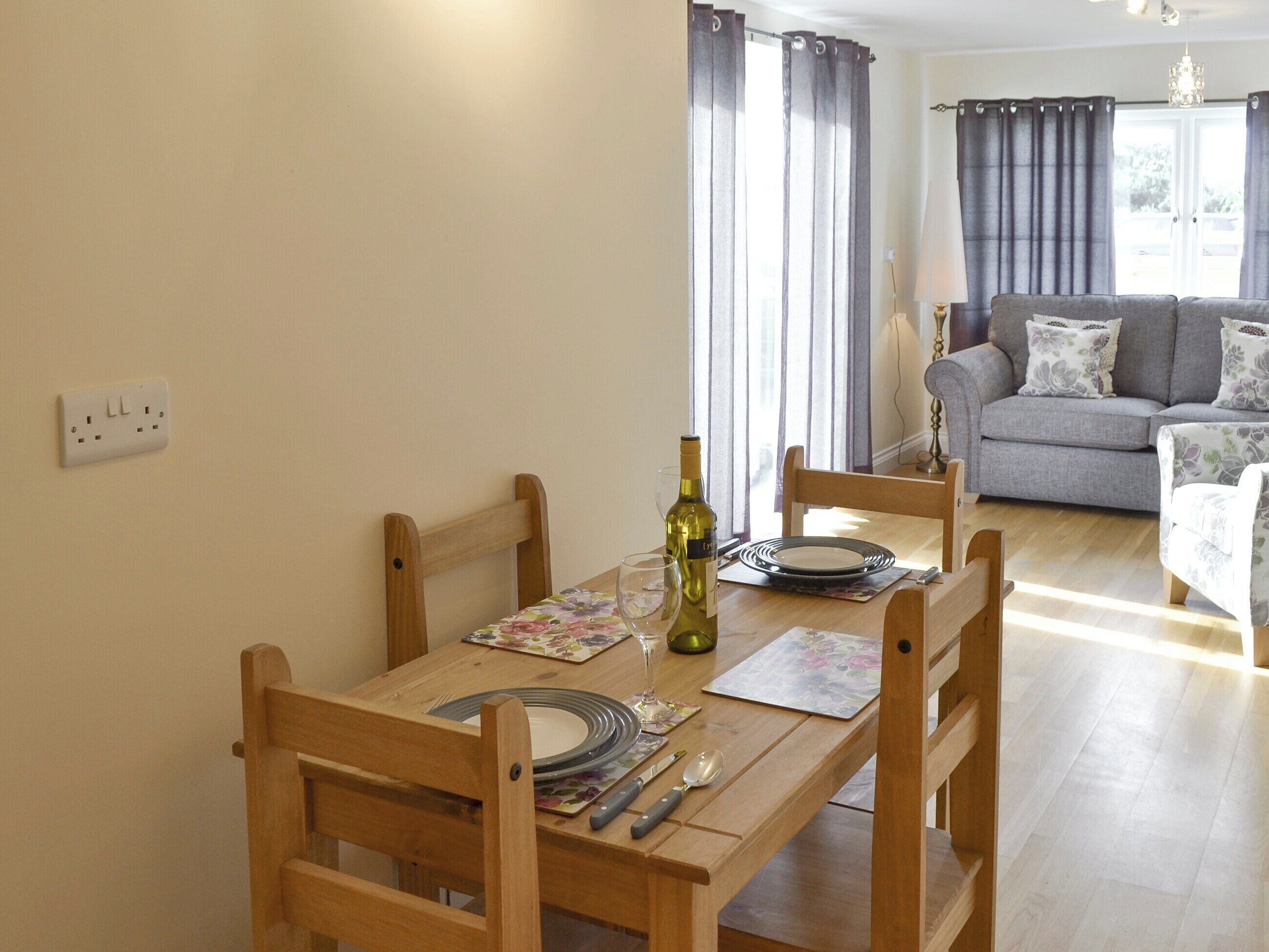 A dining area with a wooden table set for two, a bottle of wine, and a floral placemat.