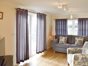 A living room with a grey sofa, floral armchairs, a lamp, and curtains on a sliding door. - 1 bedroom accommodation in Marazion (Marazion)