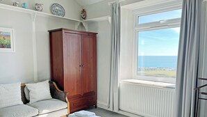 Ett sovrum med ett stort fönster, en garderob i trä, en soffa och en säng med hopvikta handdukar.