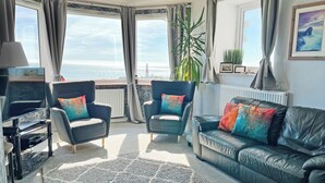 Ett vardagsrum med en soffa, två fåtöljer, en tv och utsikt över havet.