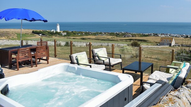Ett bubbelbad på en terrass med utsikt över havet och en fyr.