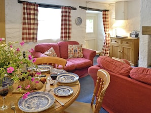A cozy living room with a red sofa, a wooden dining table set with plates and a wine glass, and a window with curtains. - 2 bedroom accommodation in Betws-y-Coed (Betws-y-Coed)