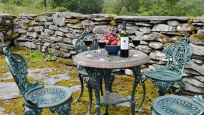 A stone wall, a round table with a bottle and glasses, and ornate green chairs. - 2 bedroom accommodation in Betws-y-Coed (Betws-y-Coed)