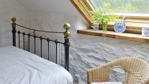 A bedroom with a bed, a wicker chair, a window with a view of greenery, and a shelf with decorative items. - 2 bedroom accommodation in Betws-y-Coed (Betws-y-Coed)