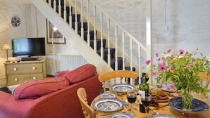 A dining area with a table set for four, a sofa, a television, and a staircase. - 2 bedroom accommodation in Betws-y-Coed (Betws-y-Coed)