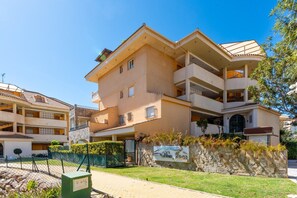 A multi-story residential building with balconies, a stone wall with a sign, and a paved walkway.