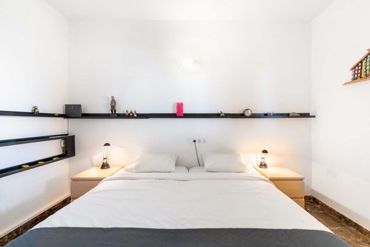 A hotel room with a bed, bedside tables, and shelves with various items.