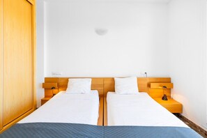 A hotel room with two single beds, wooden headboards, bedside tables with lamps, and a wardrobe.
