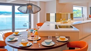 A modern kitchen with a dining area, large windows, and a view of the sea.