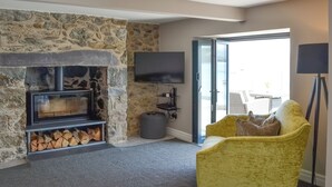 A room with a stone fireplace, a television mounted on the wall, a yellow armchair, and a view through a glass door.
