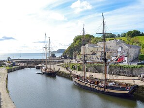 A harbor with a large sailing ship docked, a stone building, and a clear sky.