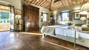 A bedroom with a large wooden wardrobe, a bed with a patterned bedspread, and a stone wall. - VILLA CHIANTIVERTINE (Vertine)