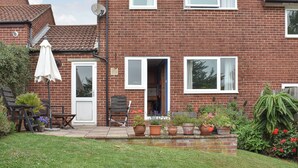 A two-story brick house with a front door, a satellite dish, and a small garden with potted plants and a white umbrella. - 3 bedroom accommodation in Preston, near Weymouth (Preston, near Weymouth)