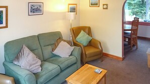 A living room with a green sofa, a brown leather armchair, a wooden coffee table, and a dining area with a wooden table and chairs. - 3 bedroom accommodation in Preston, near Weymouth (Preston, near Weymouth)