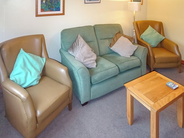 A living room with a green sofa, two brown leather armchairs, and a wooden coffee table. - 3 bedroom accommodation in Preston, near Weymouth (Preston, near Weymouth)