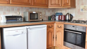 A kitchen with wooden cabinets, a Bosch dishwasher, a microwave, a toaster, a kettle, and a stove. - 3 bedroom accommodation in Preston, near Weymouth (Preston, near Weymouth)