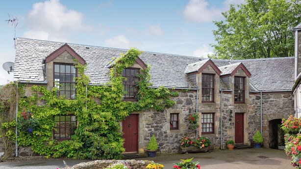 A stone building with a sloped roof, multiple windows, and a stone wall surrounding a courtyard with potted plants. - 2 bedroom accommodation in Kinross, near Perth (Kinross, near Perth)