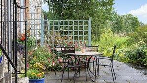 A stone-paved outdoor seating area with a table and chairs, surrounded by lush greenery and flowers. - 2 bedroom accommodation in Kinross, near Perth (Kinross, near Perth)