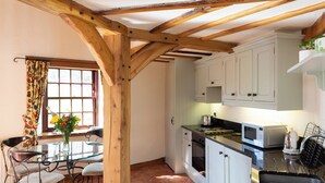 A kitchen with white cabinets, a stove, a microwave, and a sink. There is a dining table with chairs and a vase of flowers. - 2 bedroom accommodation in Kinross, near Perth (Kinross, near Perth)