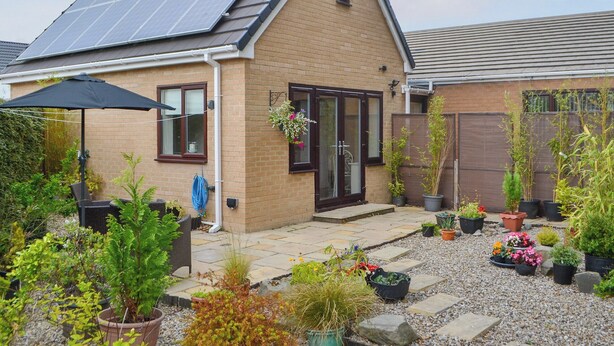 Ein Haus mit Solaranlage, einer Terrasse mit Blumentöpfen und einem Garten.
