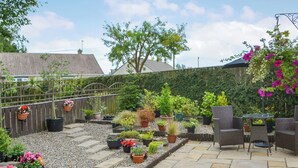 Eine Terrasse mit Steinböden, Blumentöpfen und Gartenmöbeln.