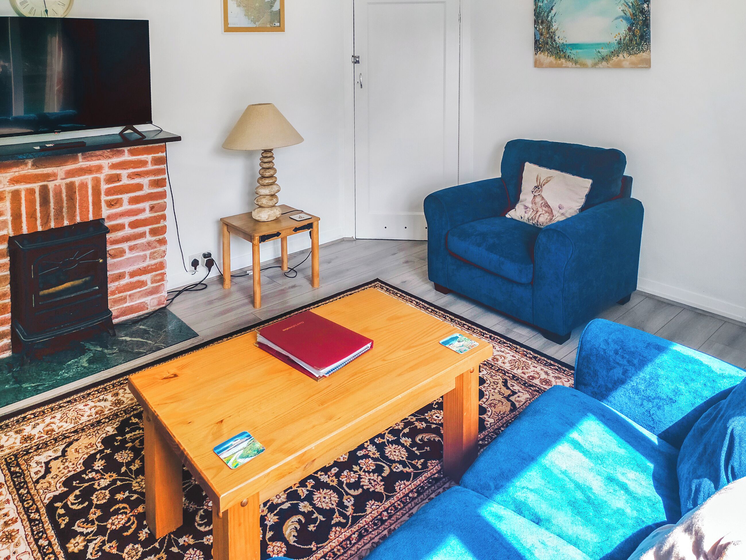 A living room with a fireplace, a blue sofa, a wooden coffee table, and a patterned rug.