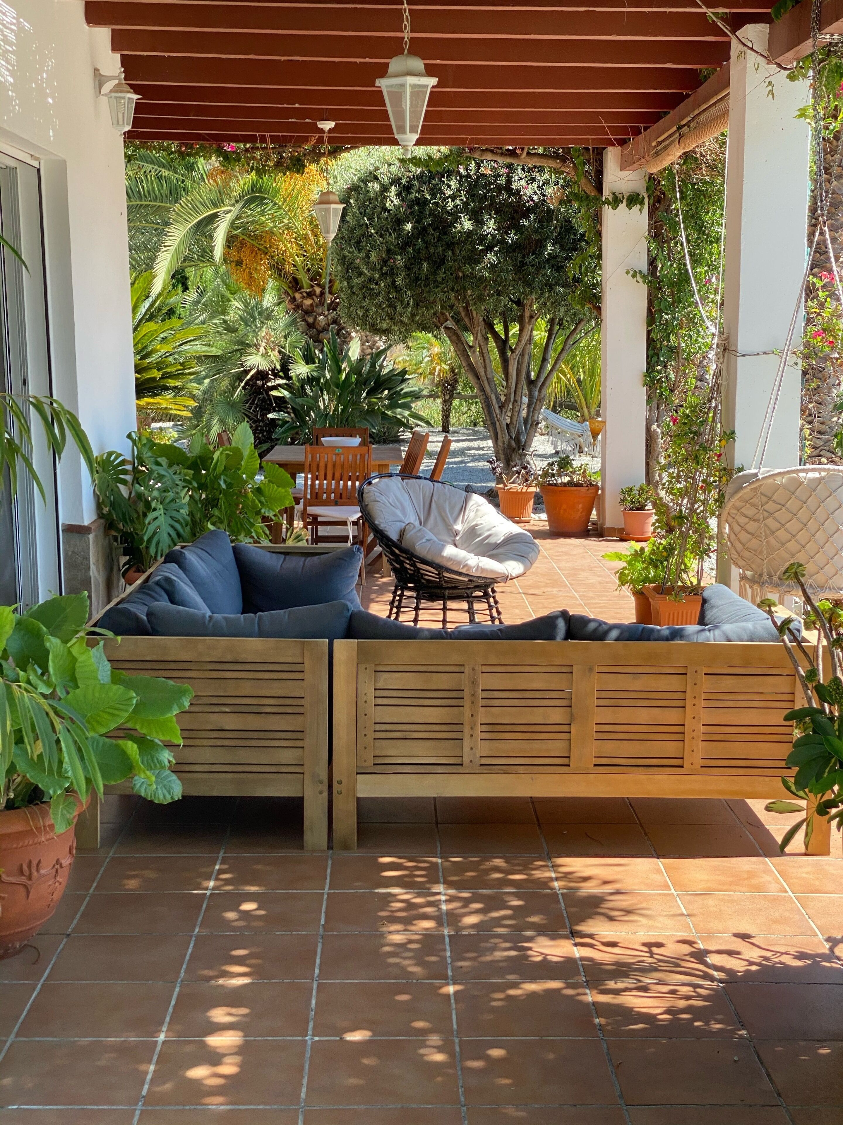 A covered patio area with a wooden bench, two lounge chairs, and potted plants.