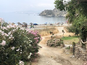 A coastal path leading to a beach with umbrellas and people.