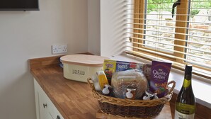A kitchen counter with a bread box, cereal boxes, a wicker basket with jars, a wine bottle, and a window with blinds. - 3 bedroom accommodation in Pendleton, near Clitheroe (Pendleton, near Clitheroe)