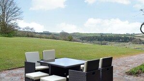 An outdoor patio with wicker furniture and a view of a grassy field and hills. - The Farmhouse - UKC1339 (Heasley Mill, near South Molton)