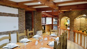 A dining area with a long wooden table set for a meal, surrounded by brick walls and wooden beams. - The Farmhouse - UKC1339 (Heasley Mill, near South Molton)