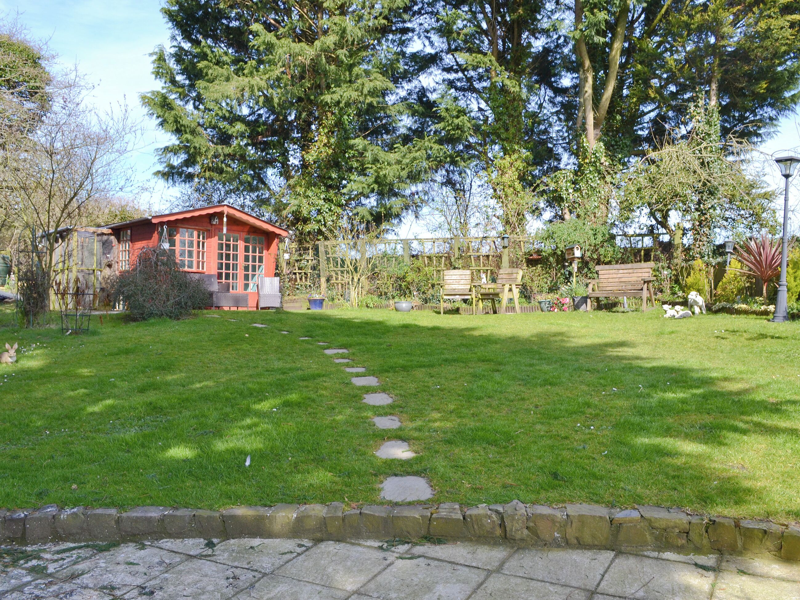 Ein rotes Gebäude mit einem Gartenweg, der davor führt, umgeben von Bäumen und einer Bank.