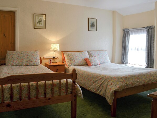 Une chambre avec deux lits, une table de chevet avec une lampe et une fenêtre avec des rideaux.