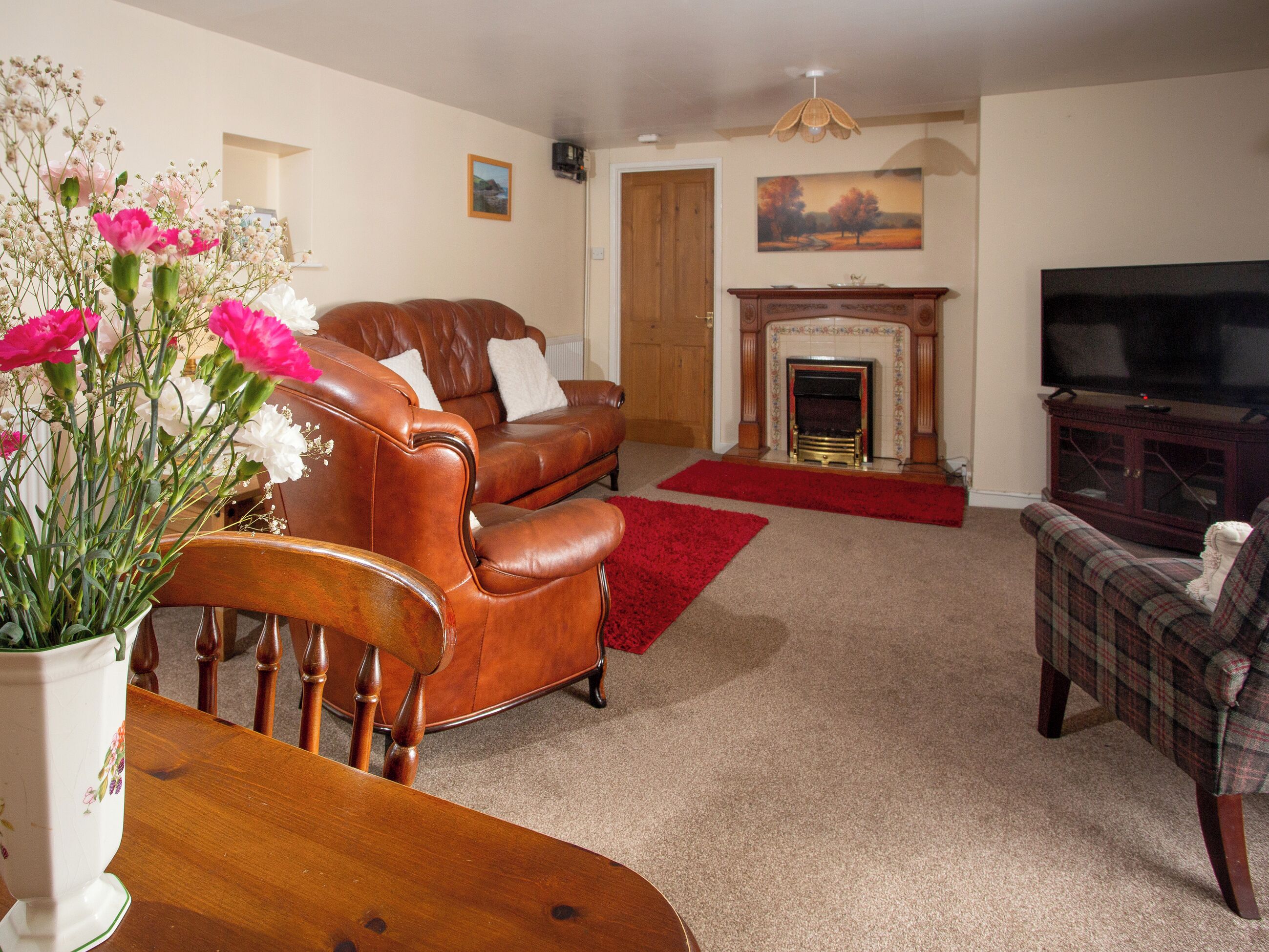 A living room with a fireplace, a television, and a dining area with a vase of flowers.
