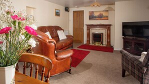 Una sala de estar con chimenea, televisor y comedor con un jarrón de flores.