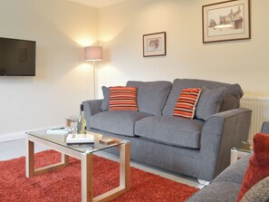 A living room with a grey sofa, red and white striped pillows, a glass coffee table, and a red carpet.