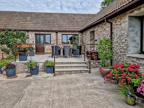 A stone building with a tiled roof, outdoor seating area with chairs and tables, and potted plants.